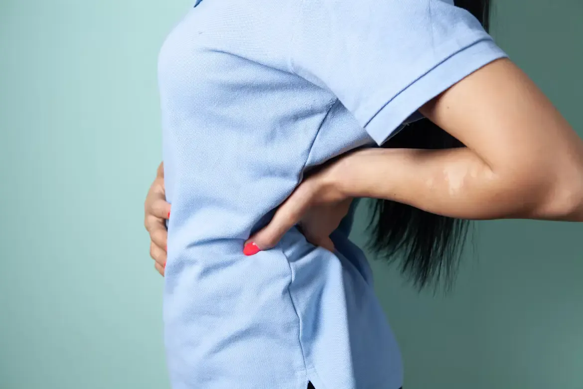 Woman in a light blue shirt holding her lower back and side with both hands